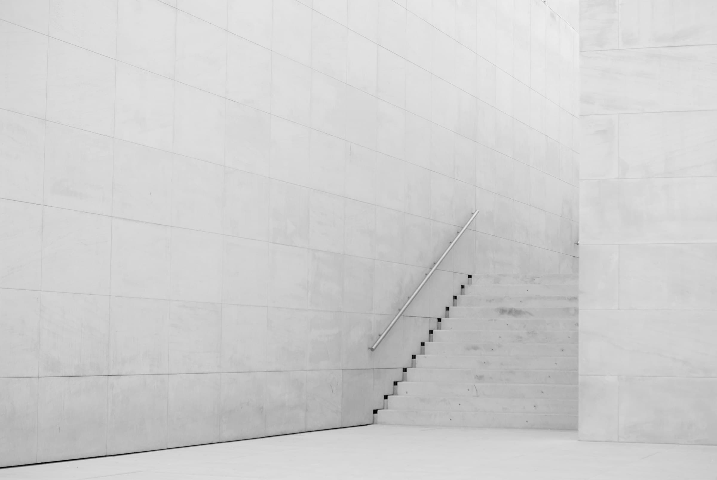 A single handrail against a plain concrete stairway.